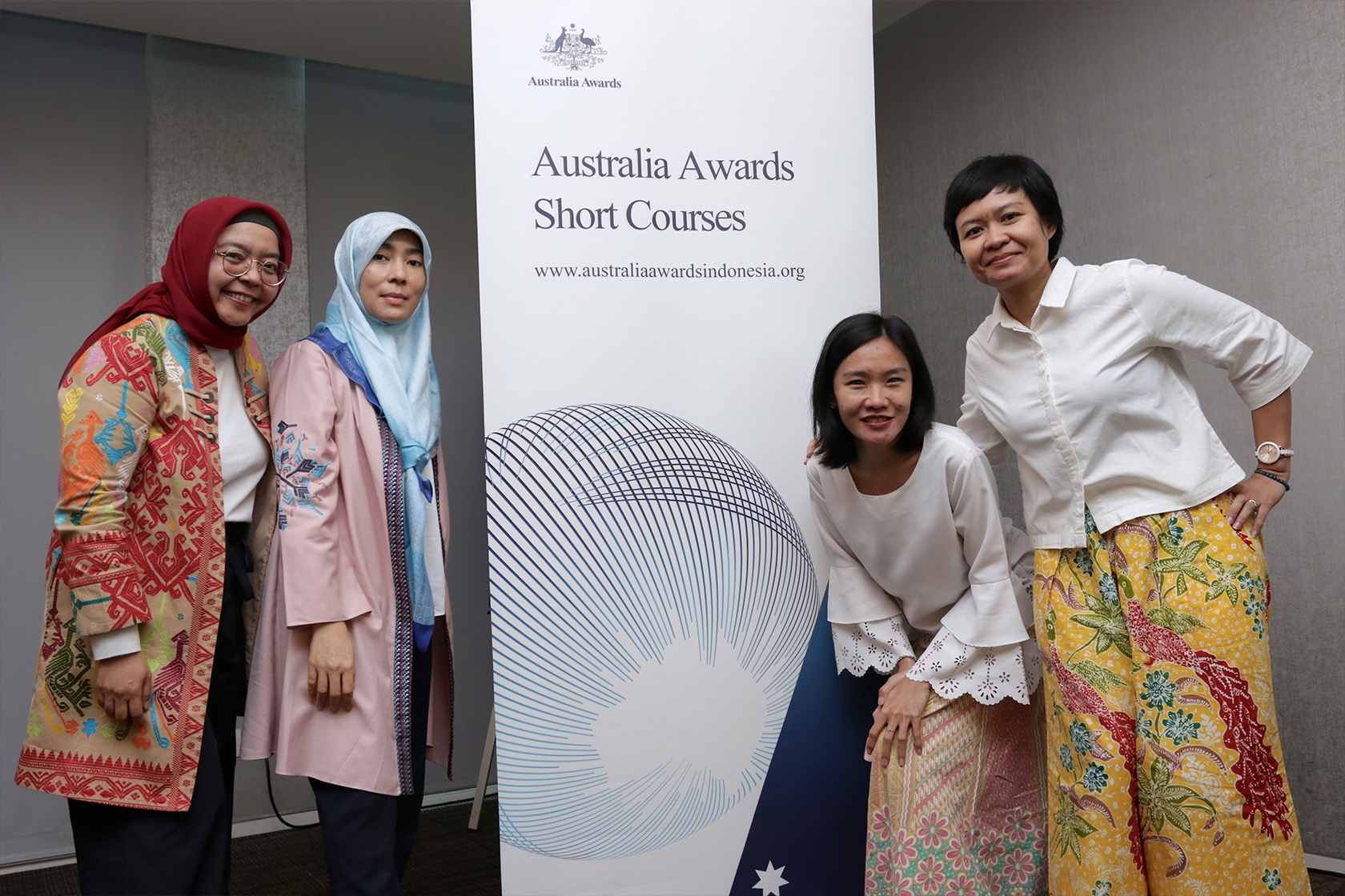 Cuatro graduados están de pie y posan con la pancarta de pie para el Curso Corto de los Premios de Australia